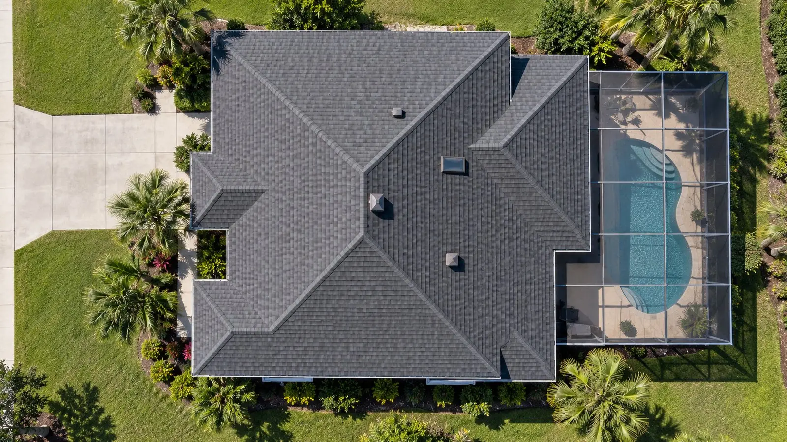 Straight-down aerial view of the shingle hip roof of a Florida home, driveway, lawn and pool enclosure